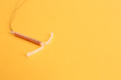 Photo of Copper intrauterine contraceptive device on yellow background. Space for text