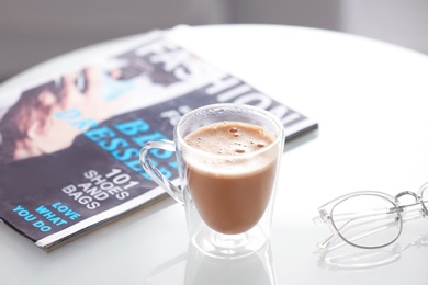 Cup of aromatic coffee and magazine on table