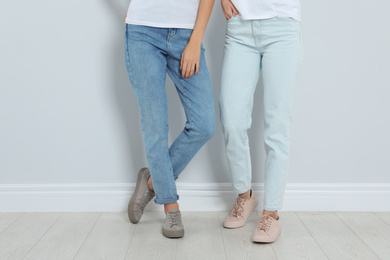 Photo of Young women in stylish jeans near light wall, closeup
