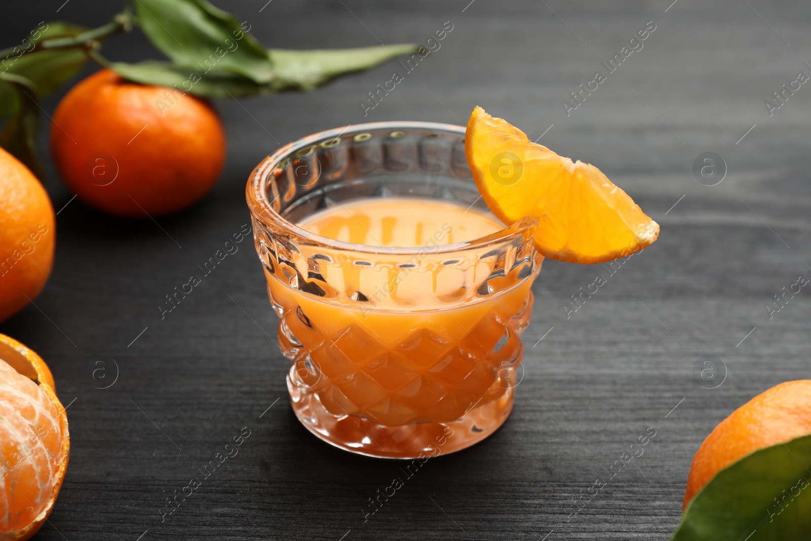 Photo of Tasty tangerine liqueur in glass and fresh fruits on black wooden table