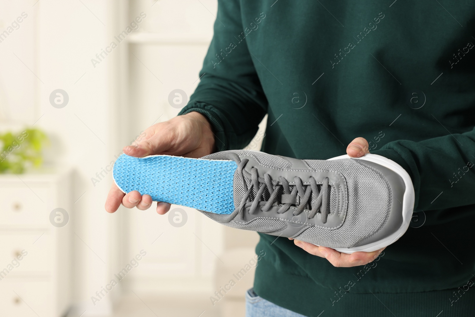 Photo of Man putting orthopedic insole into shoe indoors, closeup