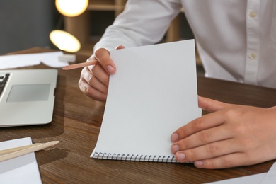 Man with pencil and notepad at wooden table, closeup
