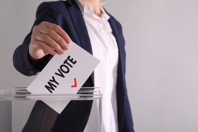 Woman putting paper with text My Vote and tick into ballot box on light grey background