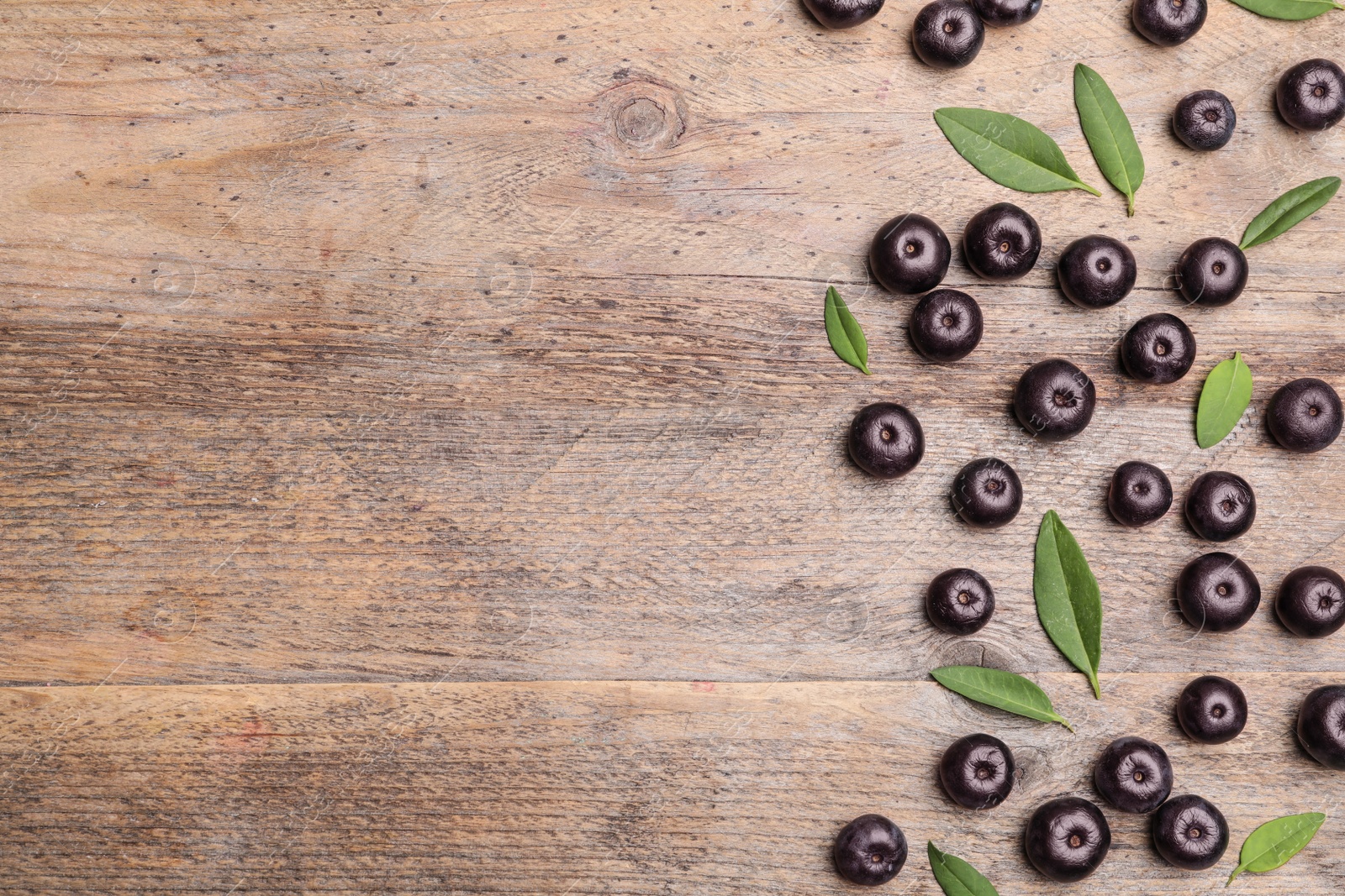 Photo of Fresh acai berries with leaves on wooden table, flat lay. Space for text