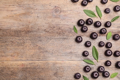 Photo of Fresh acai berries with leaves on wooden table, flat lay. Space for text