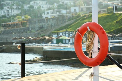 Photo of Orange lifebuoy hanging on post near sea, space for text