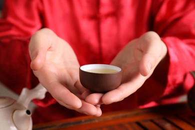 Photo of Master offering cup of freshly brewed tea during traditional ceremony at table, closeup