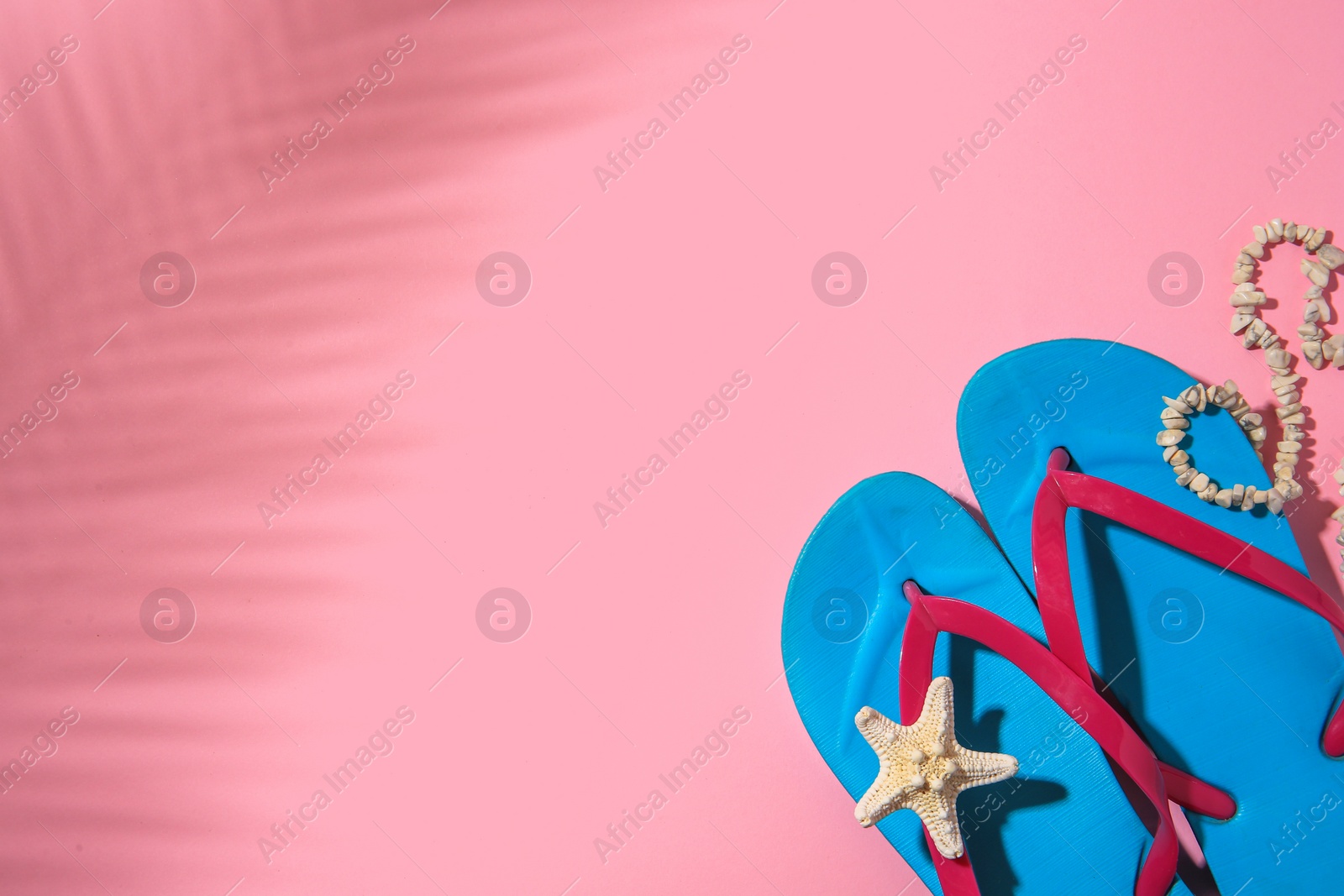 Photo of Light blue flip flops, starfish and necklace on pink background, top view with space for text. Beach accessories
