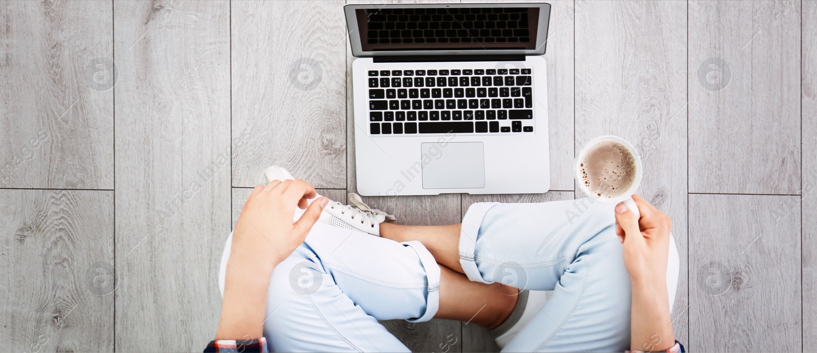 Image of Young man with cup of coffee working on computer indoors, top view. Banner design