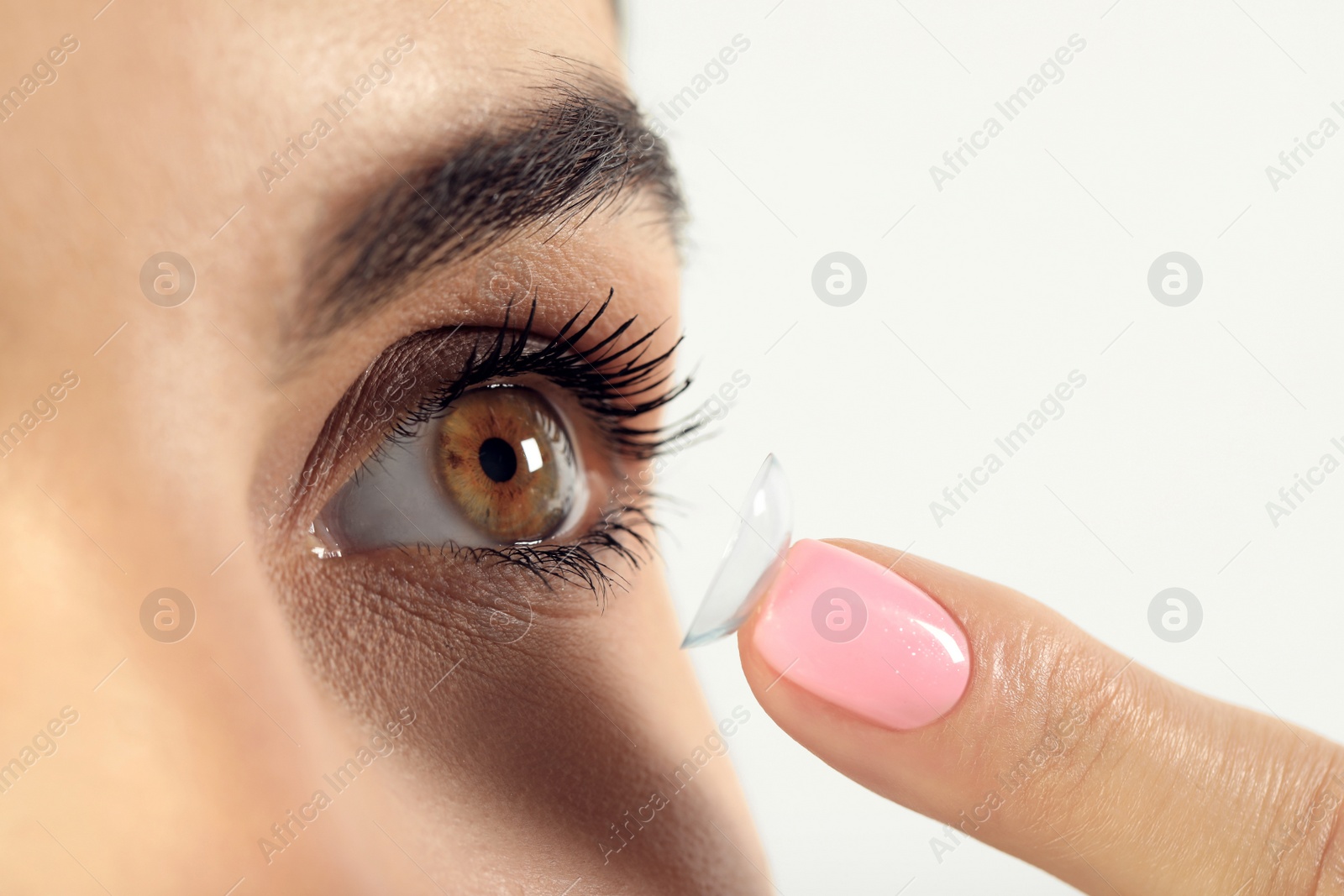 Photo of Young woman putting contact lens in her eye, closeup