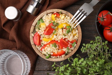Cooked bulgur with vegetables in bowl on wooden table, flat lay