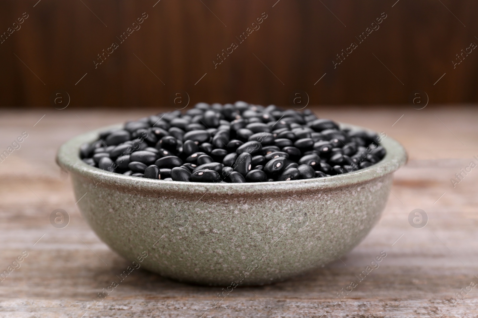 Photo of Bowl of raw black beans on wooden table, closeup