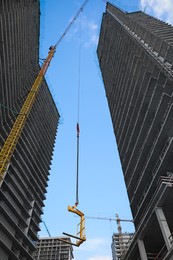 Photo of Tower crane near unfinished buildings against cloudy sky on construction site, low angle view