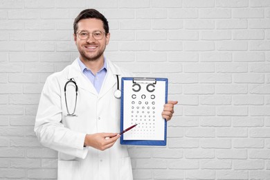 Ophthalmologist pointing at vision test chart near white brick wall. Space for text