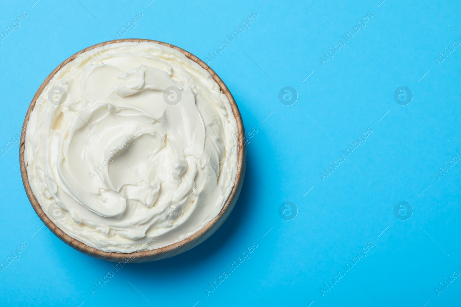 Photo of Bowl of tasty cream cheese on light blue background, top view. Space for text