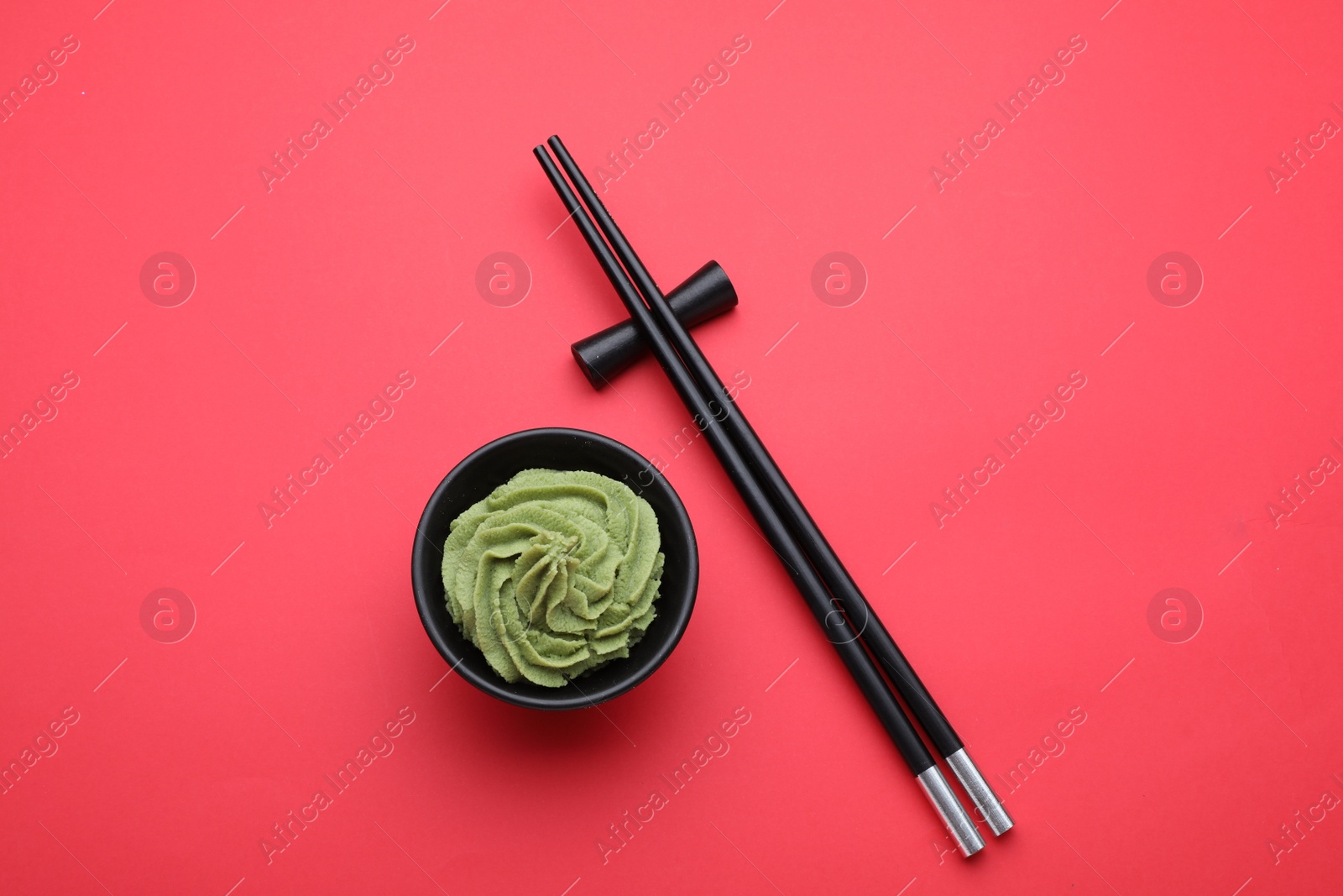 Photo of Bowl with swirl of wasabi paste and chopsticks on red background, flat lay