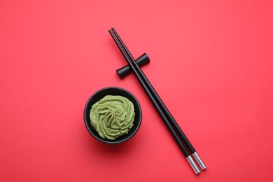 Photo of Bowl with swirl of wasabi paste and chopsticks on red background, flat lay