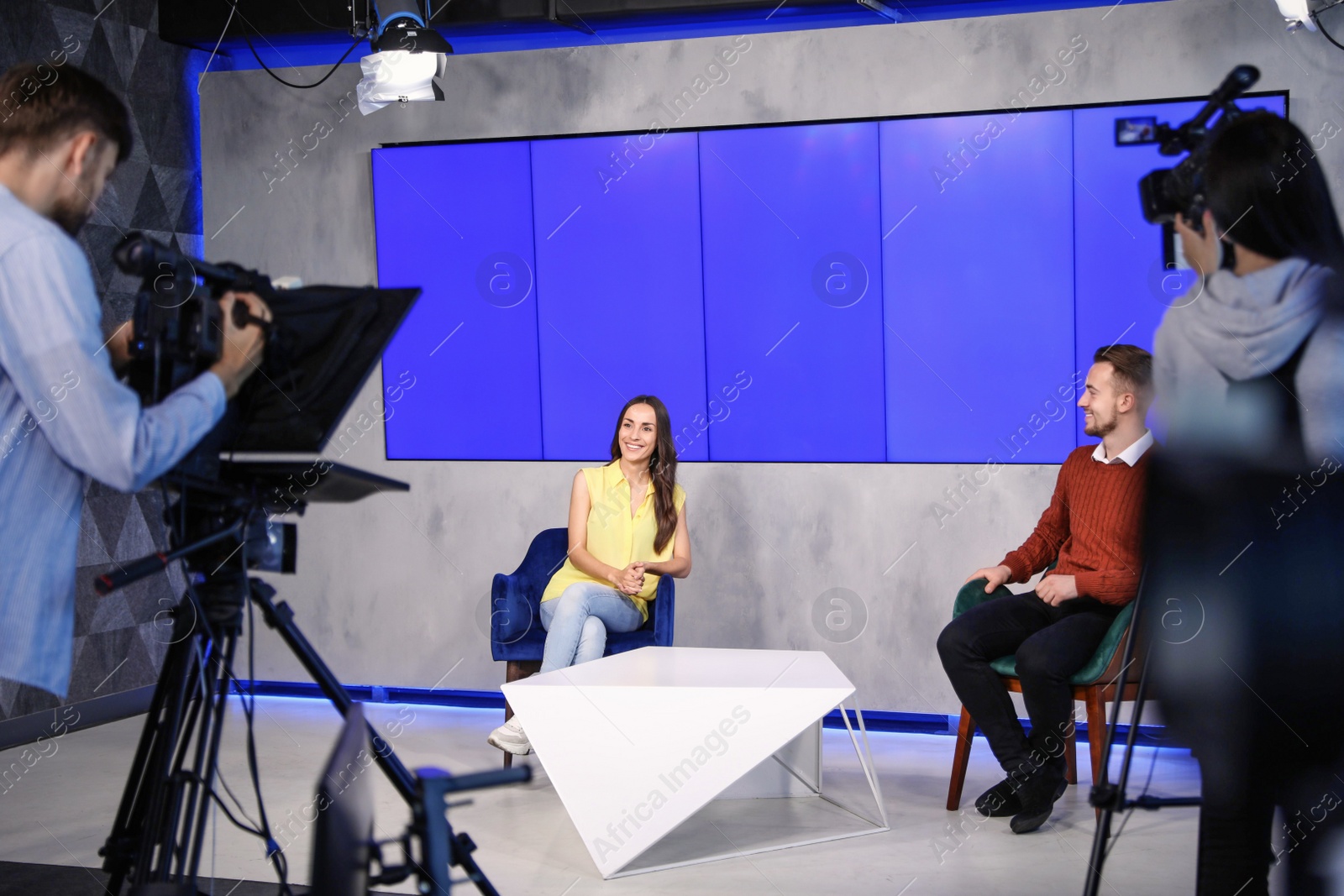 Photo of Presenters and video camera operator working in studio. News broadcasting