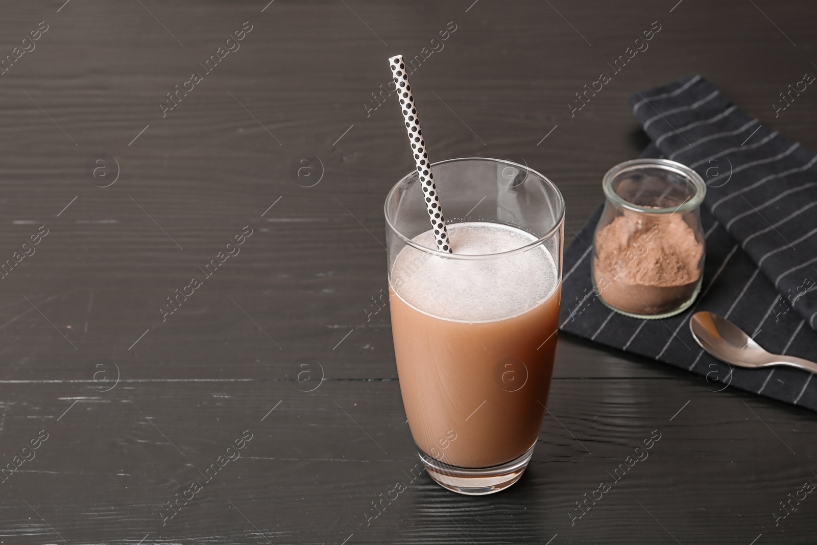 Photo of Glass of chocolate protein shake on black wooden table. Space for text