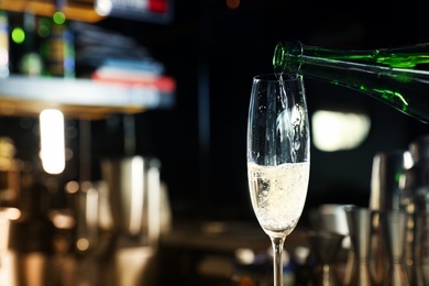 Pouring champagne from bottle into glass in bar. Space for text