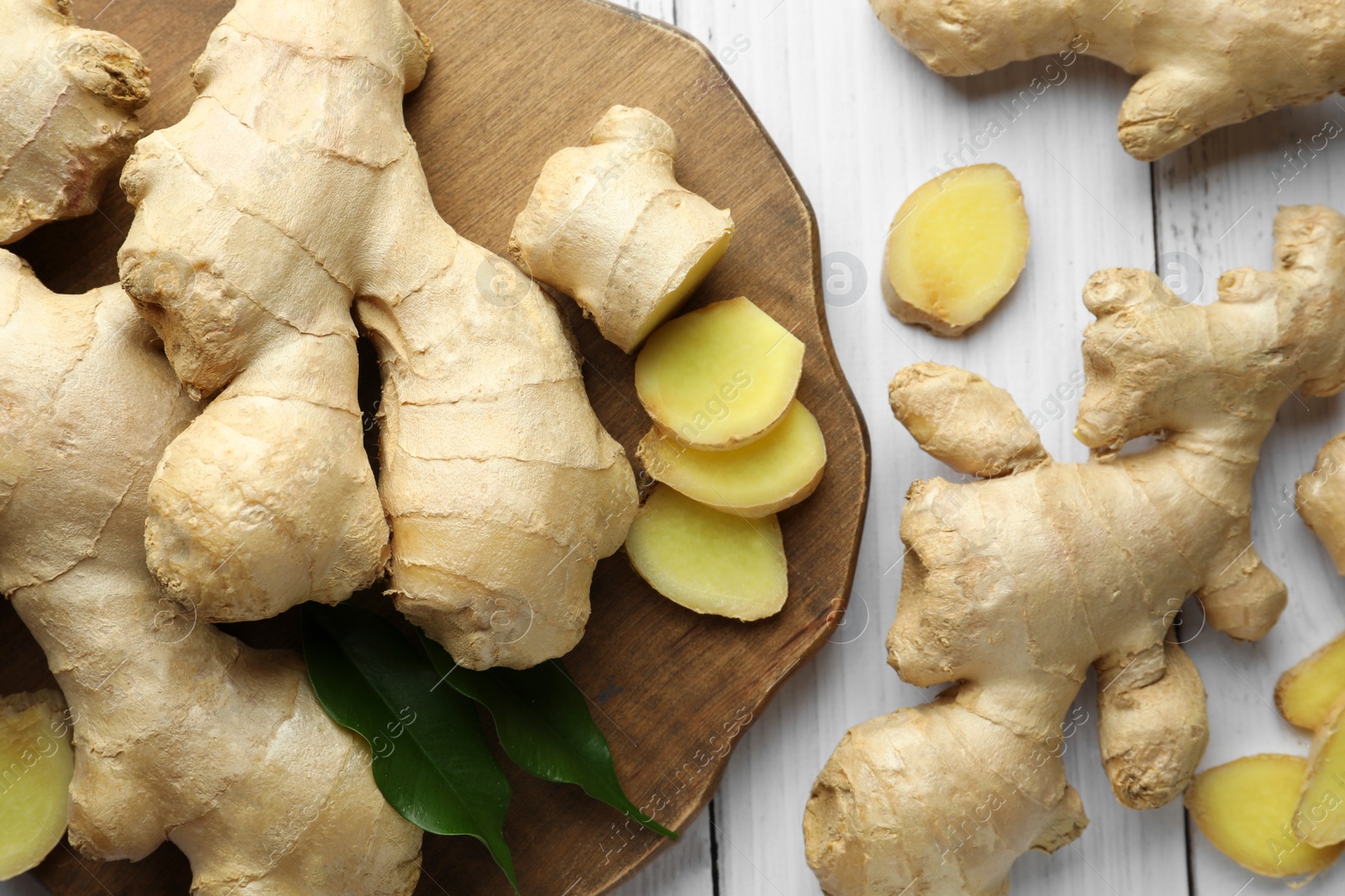 Photo of Cut and whole fresh ginger with leaves on white wooden table, flat lay