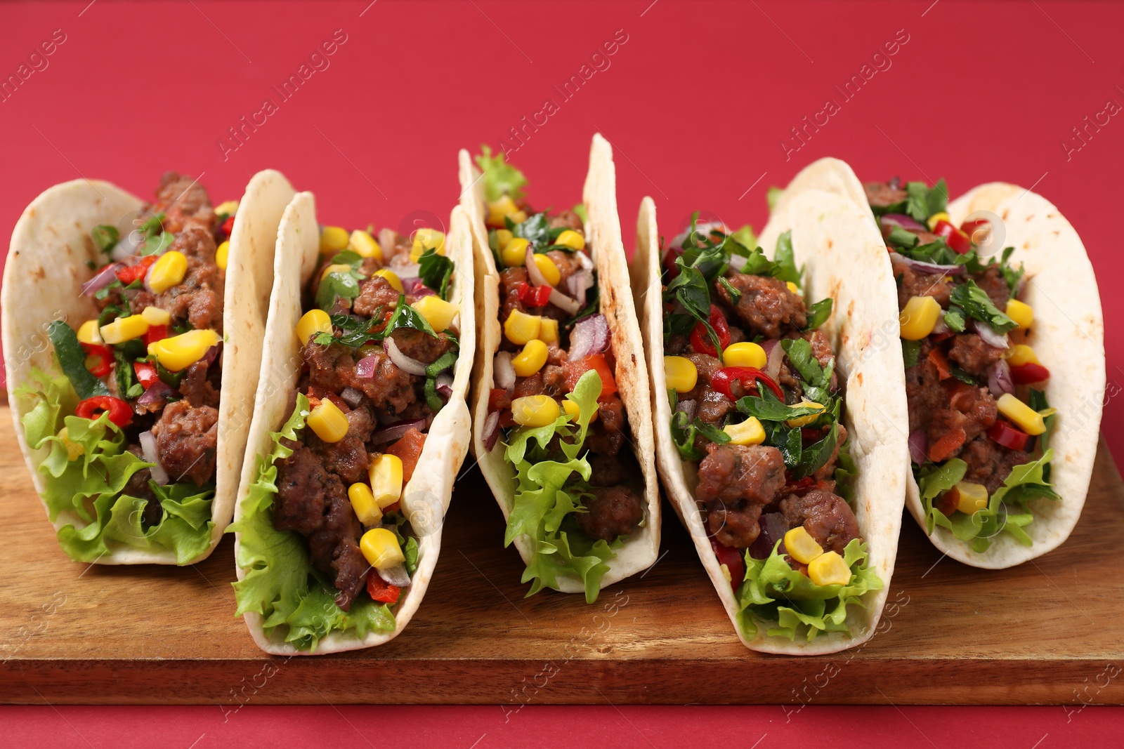 Photo of Delicious tacos with meat and vegetables on red table, closeup