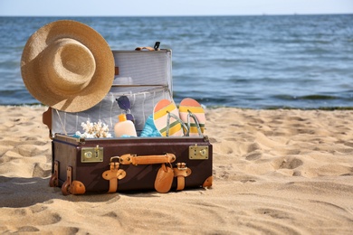 Photo of Open suitcase with stylish beach accessories on sand near sea. Space for text