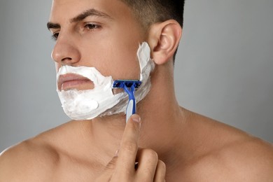 Photo of Handsome man shaving with razor on grey background, closeup