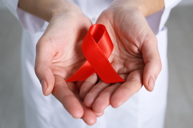 Photo of Woman holding red awareness ribbon on grey background, closeup. World AIDS disease day