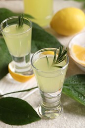 Photo of Tasty limoncello liqueur with rosemary and green leaves on table, closeup