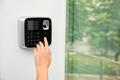 Photo of Young woman entering code on alarm system keypad indoors