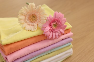 Photo of Stack of clean clothes and flowers on wooden table, closeup