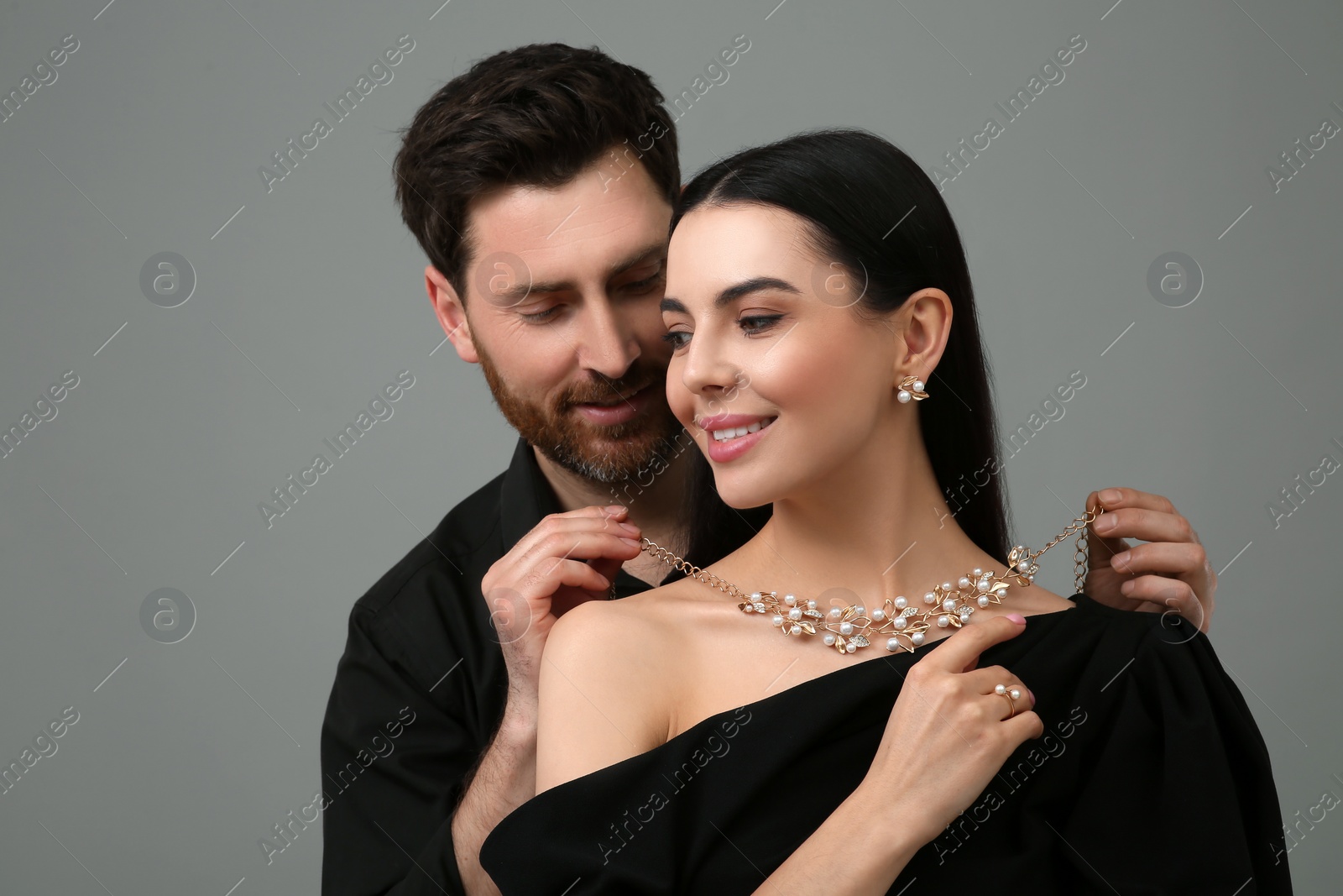 Photo of Man putting elegant necklace on beautiful woman against grey background