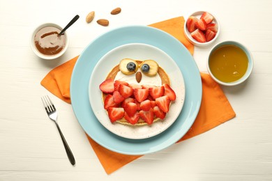 Photo of Creative serving for kids. Plate with cute owl made of pancakes, strawberries, cream, banana and almond on white wooden table, flat lay