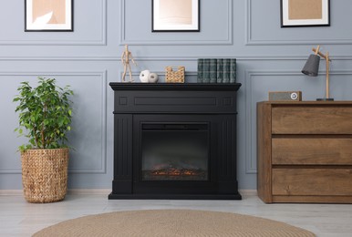Photo of Black stylish fireplace between potted plant and chest of drawers in cosy living room