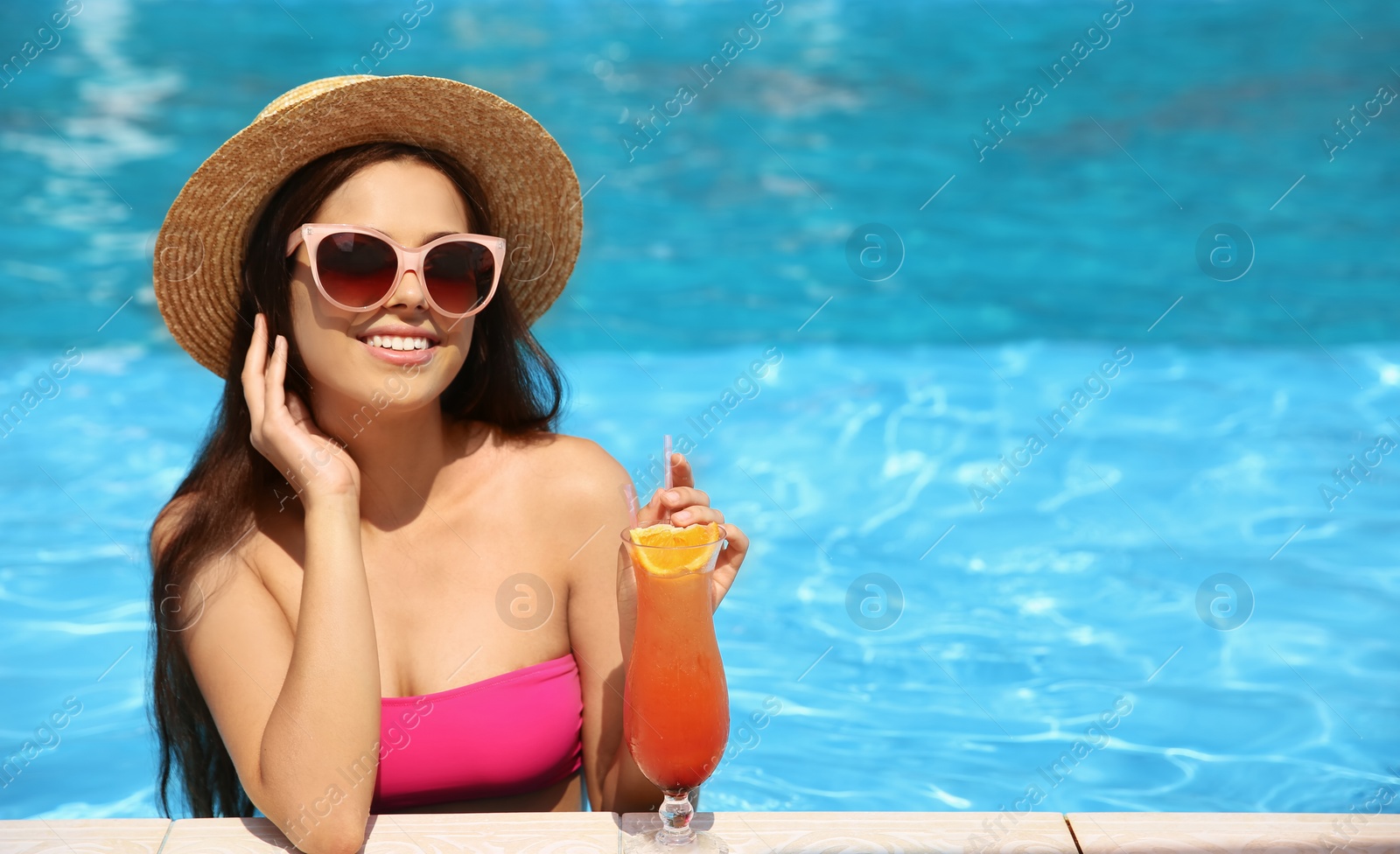 Photo of Beautiful young woman with cocktail in blue swimming pool