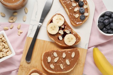 Photo of Toasts with tasty nut butter, banana slices, blueberries and peanuts on white table, flat lay