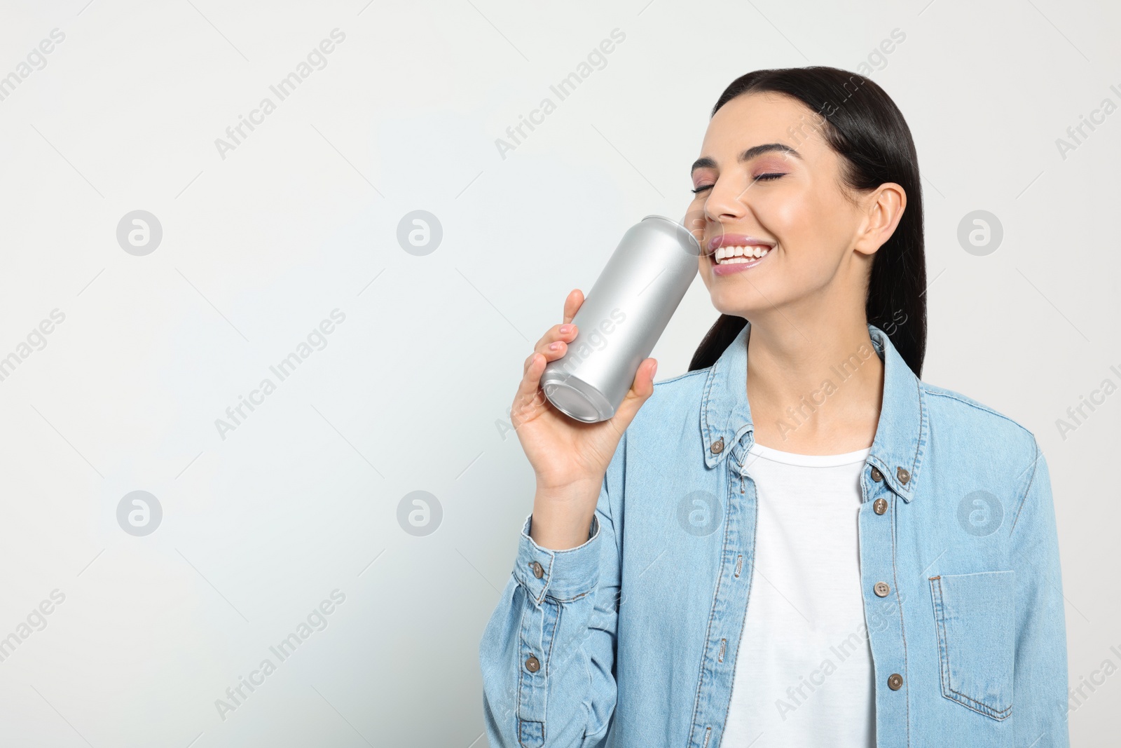 Photo of Beautiful happy woman drinking from beverage can on light grey background. Space for text