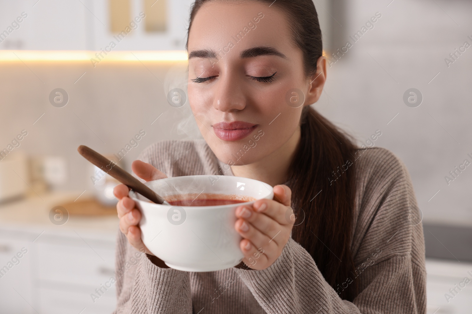 Photo of Woman with bowl of tasty tomato soup in kitchen