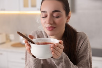 Photo of Woman with bowl of tasty tomato soup in kitchen