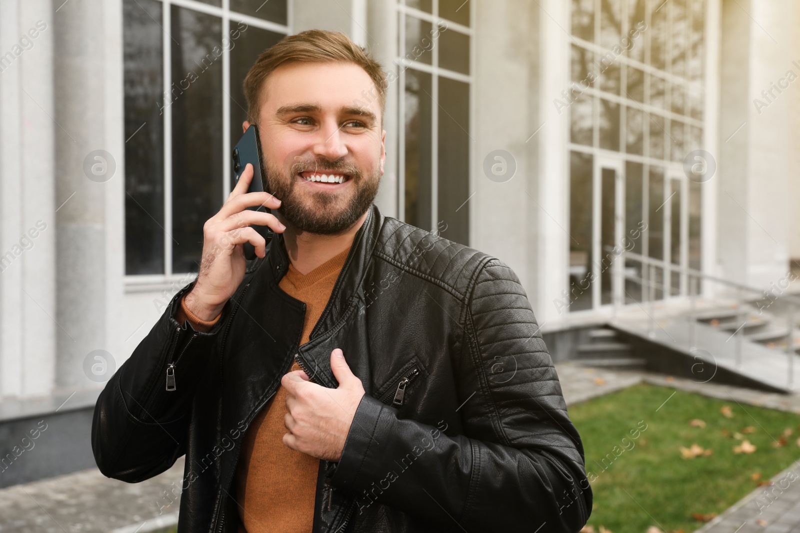 Photo of Handsome man in stylish leather jacket talking on mobile phone outdoors