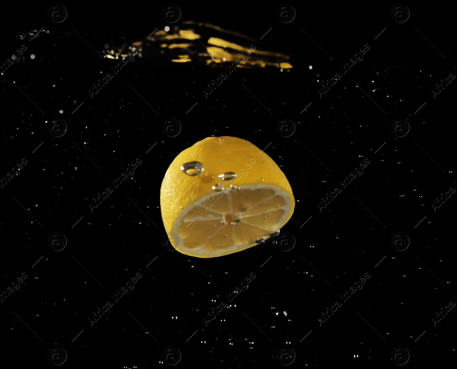 Photo of Lemon half falling down into clear water against black background