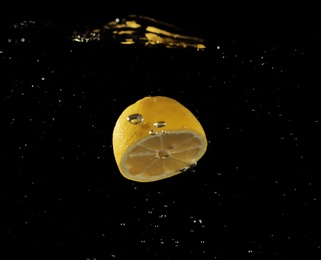 Lemon half falling down into clear water against black background