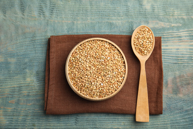 Photo of Uncooked green buckwheat grains on light blue wooden table, flat lay