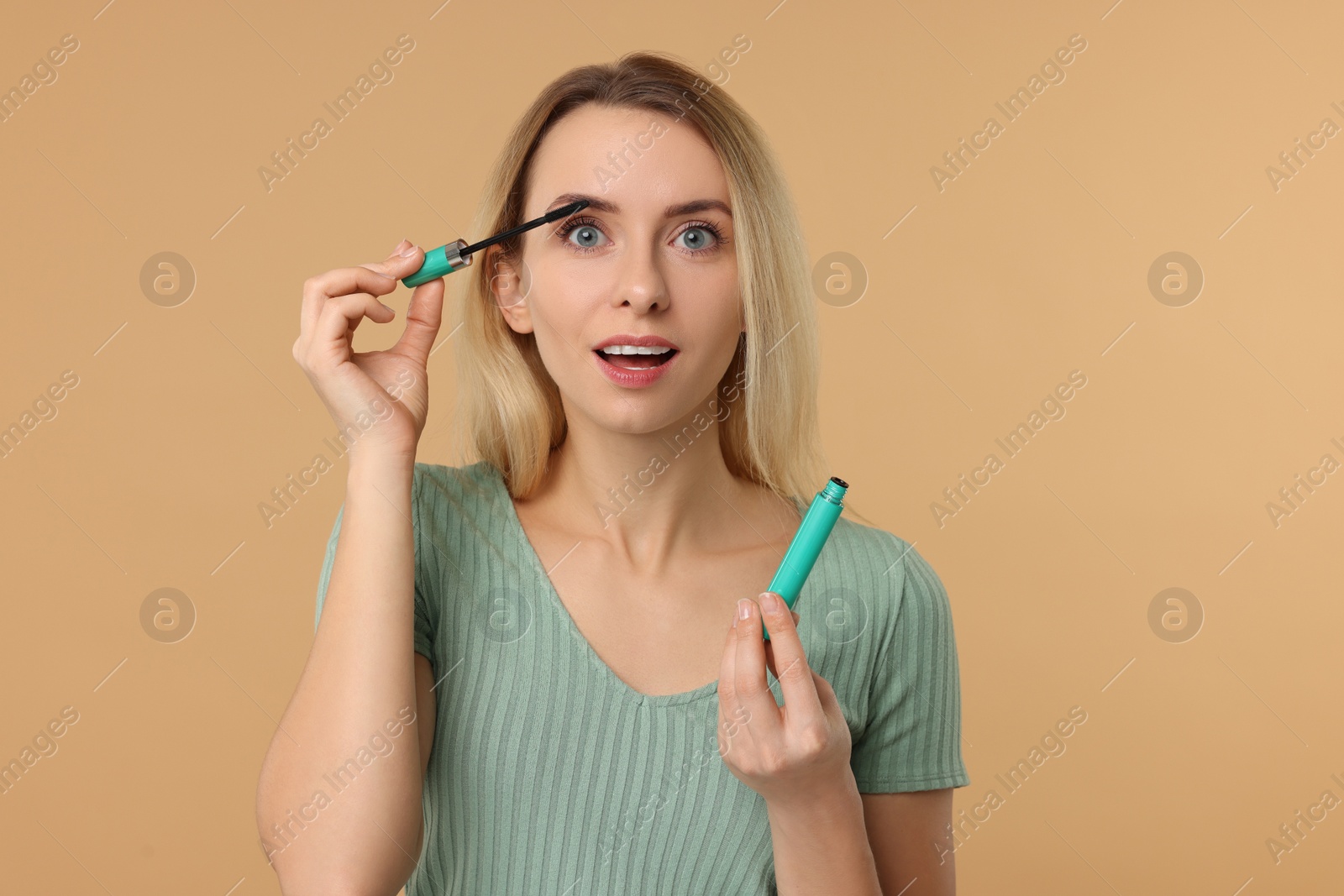 Photo of Beautiful woman applying mascara on beige background