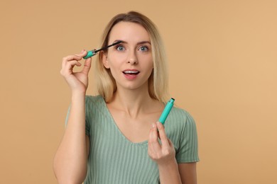 Beautiful woman applying mascara on beige background