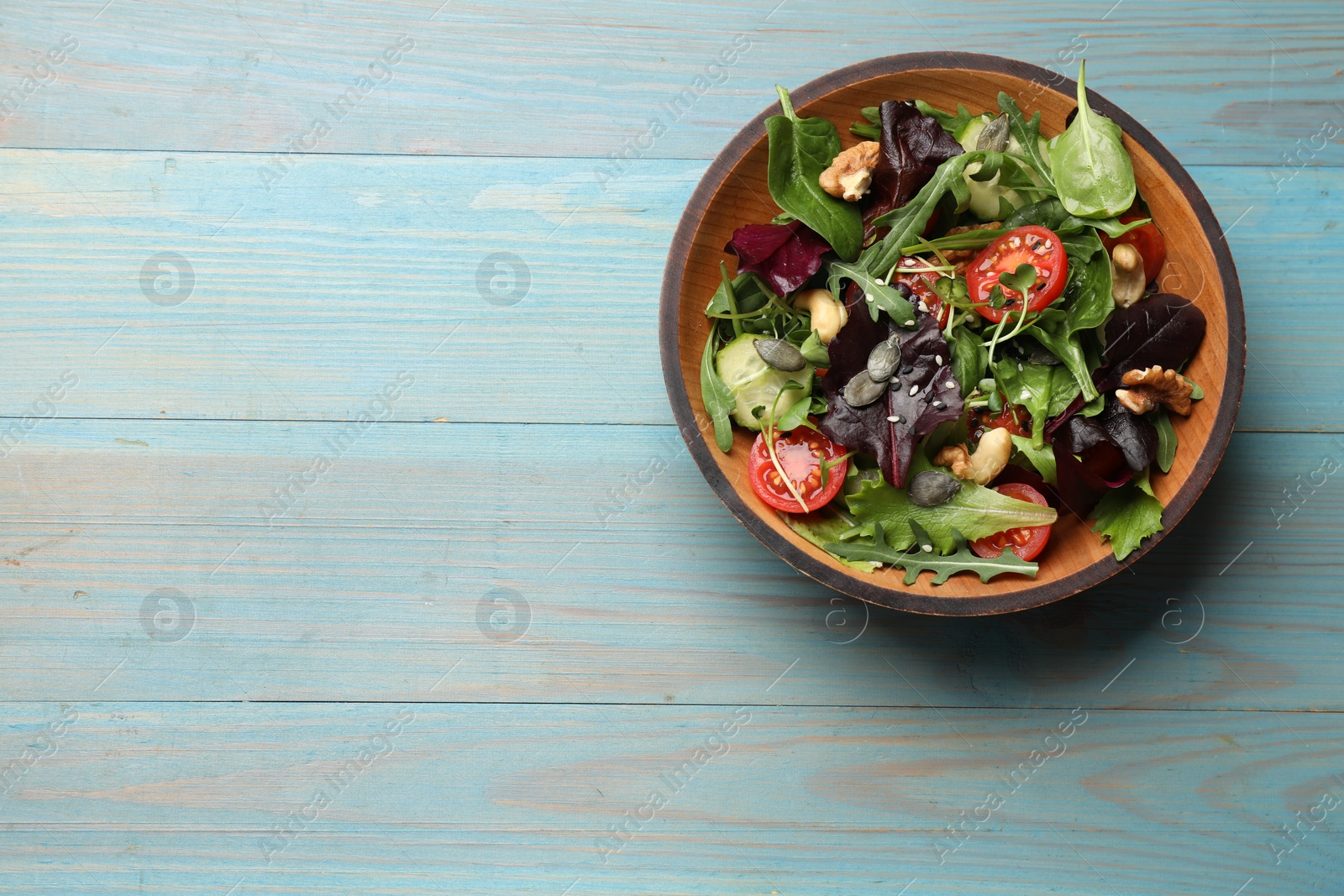 Photo of Tasty fresh vegetarian salad on light blue wooden table, top view. Space for text