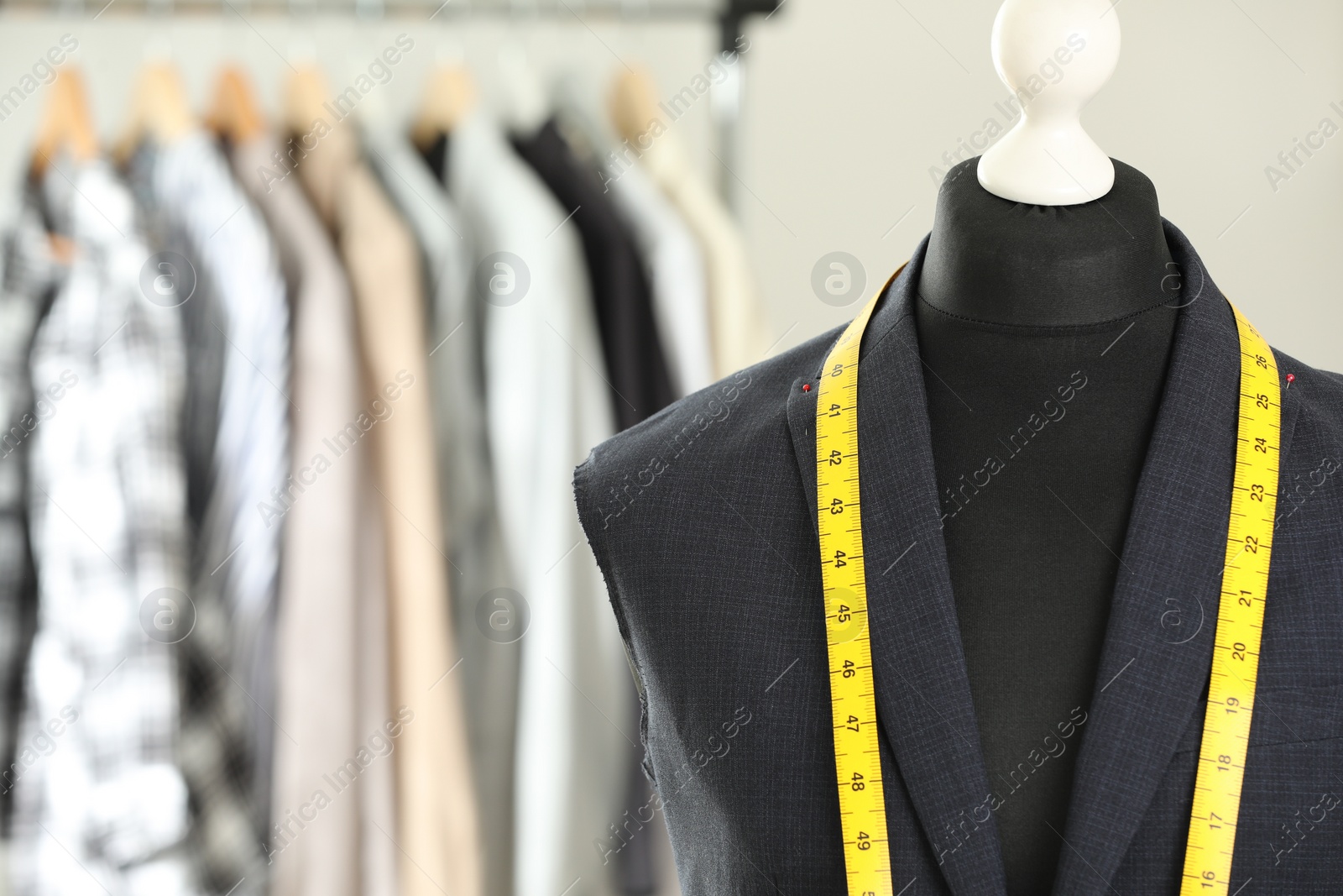 Photo of Mannequin with unfinished jacket and measuring tape in tailor shop, closeup. Space for text