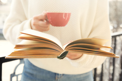 Photo of Woman with cup of coffee reading book outdoors, closeup