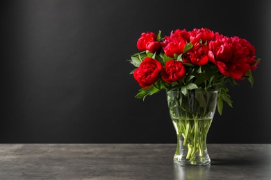 Photo of Vase with beautiful blooming peonies on table against black background